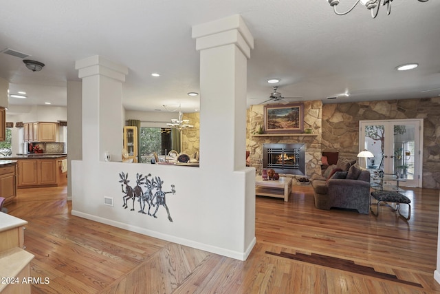 living room with a stone fireplace, light hardwood / wood-style floors, and ornate columns