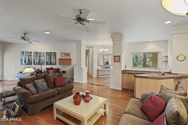 living room featuring ornate columns, sink, ceiling fan with notable chandelier, and light wood-type flooring