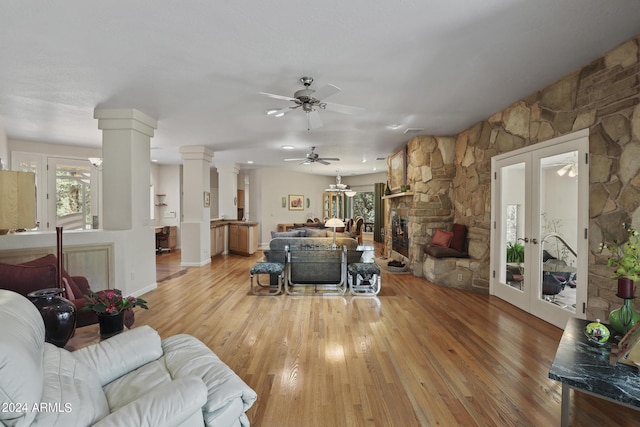 living room featuring ornate columns, a stone fireplace, ceiling fan, light hardwood / wood-style floors, and french doors