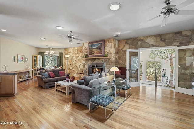 living room featuring a stone fireplace, sink, ceiling fan with notable chandelier, and light hardwood / wood-style floors