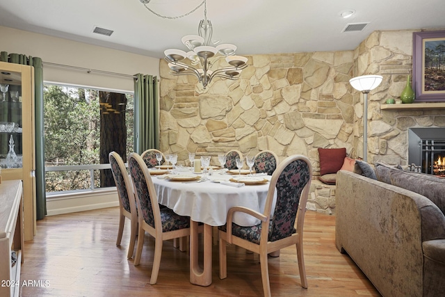 dining area featuring light wood-type flooring, a notable chandelier, and a fireplace