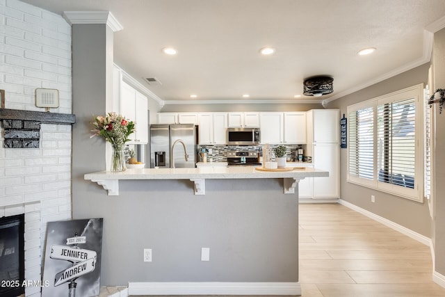 kitchen featuring a breakfast bar area, stainless steel appliances, a peninsula, decorative backsplash, and crown molding