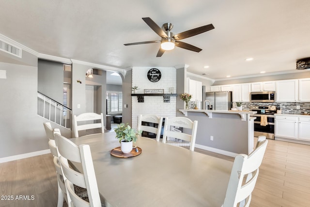 dining room featuring light wood finished floors, a brick fireplace, visible vents, and crown molding