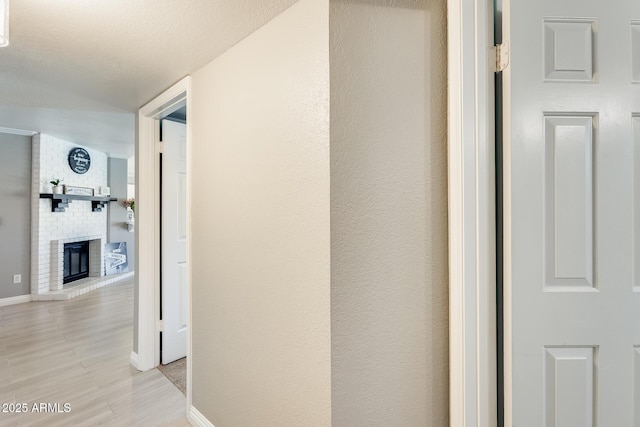 corridor with light wood-style floors, a textured ceiling, and baseboards