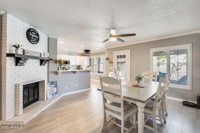 dining room with a brick fireplace, a healthy amount of sunlight, crown molding, and light wood finished floors