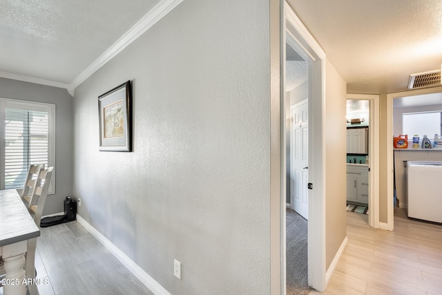 corridor with light wood finished floors, washer / clothes dryer, visible vents, ornamental molding, and baseboards