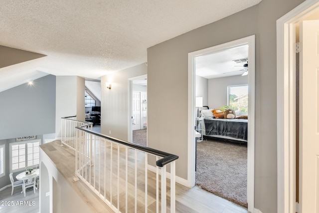 hall with a textured ceiling, visible vents, light wood-style floors, an upstairs landing, and baseboards