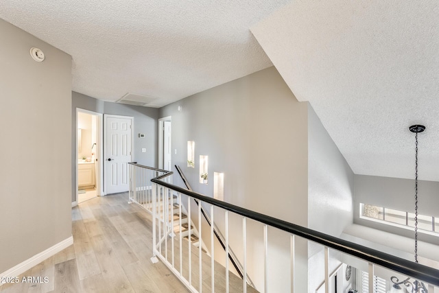 hall with light wood finished floors, a wealth of natural light, a textured ceiling, an upstairs landing, and baseboards