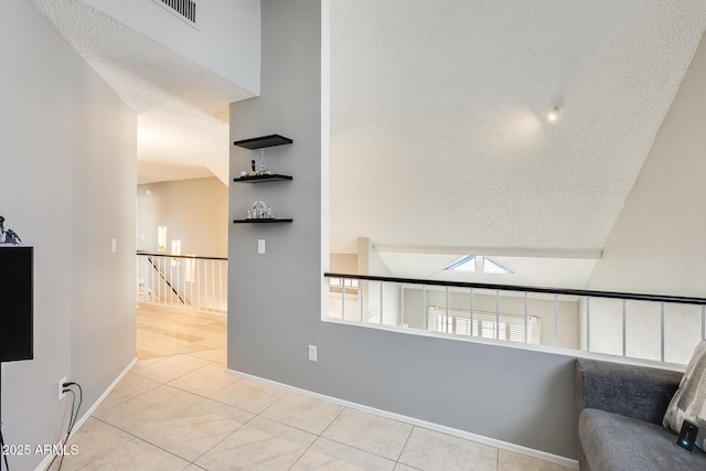 interior space with a textured ceiling, tile patterned flooring, visible vents, an upstairs landing, and baseboards