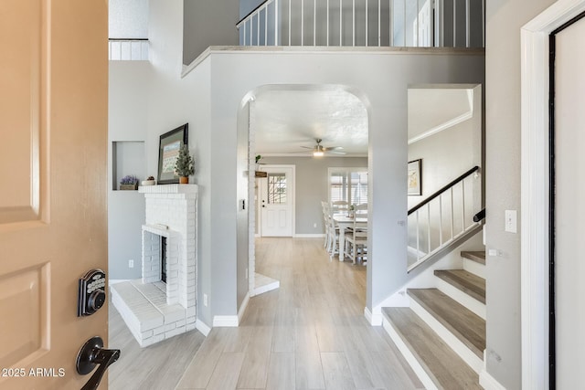 foyer with stairs, a brick fireplace, baseboards, and wood finished floors