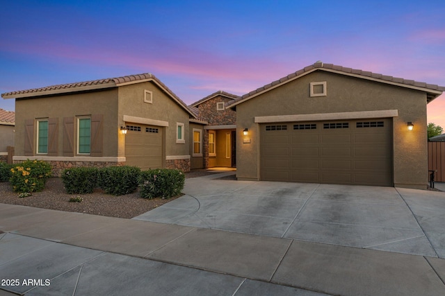view of front of property featuring a tiled roof, a garage, concrete driveway, stone siding, and stucco siding