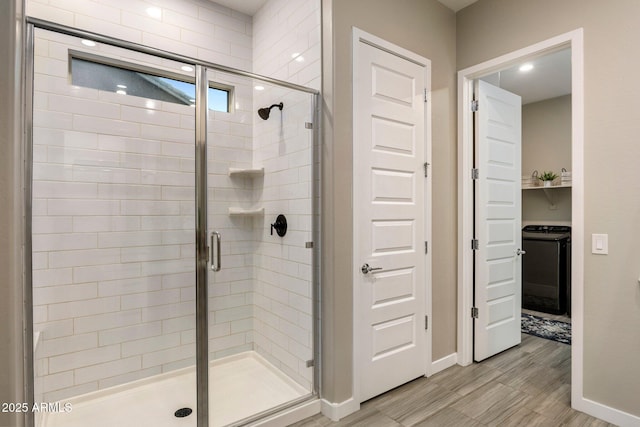 full bathroom with washer / clothes dryer, baseboards, a shower stall, and wood finished floors