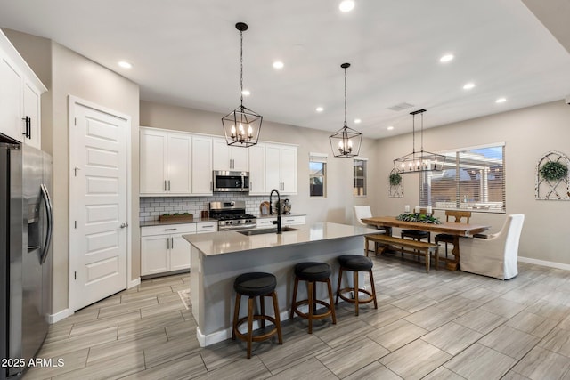 kitchen with visible vents, wood tiled floor, tasteful backsplash, a sink, and stainless steel appliances
