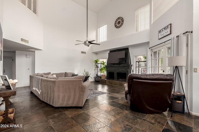 living room with ceiling fan, a towering ceiling, and a tile fireplace