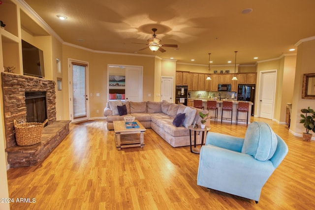 living room with ornamental molding, ceiling fan, a stone fireplace, light wood-type flooring, and baseboards