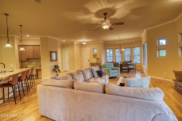 living area featuring ornamental molding, baseboards, light wood finished floors, and ceiling fan with notable chandelier