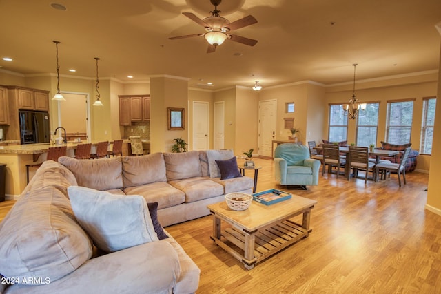 living room with recessed lighting, light wood-style floors, ornamental molding, baseboards, and ceiling fan with notable chandelier