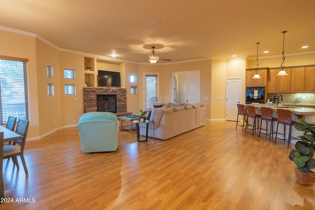 living room featuring baseboards, a stone fireplace, ornamental molding, and light wood-style floors