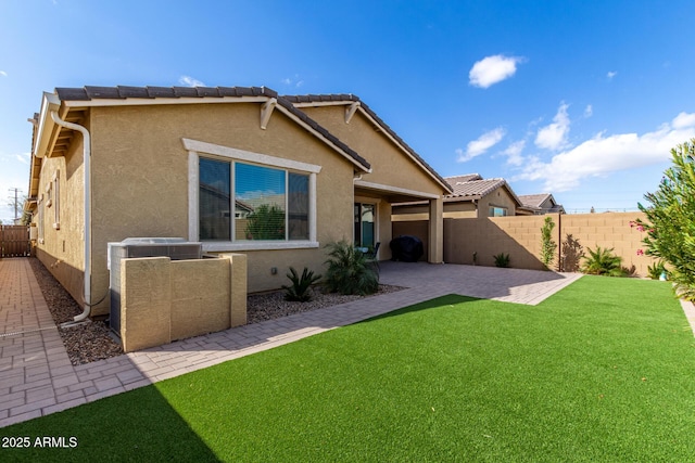 back of property featuring a patio, a yard, a fenced backyard, stucco siding, and a tiled roof