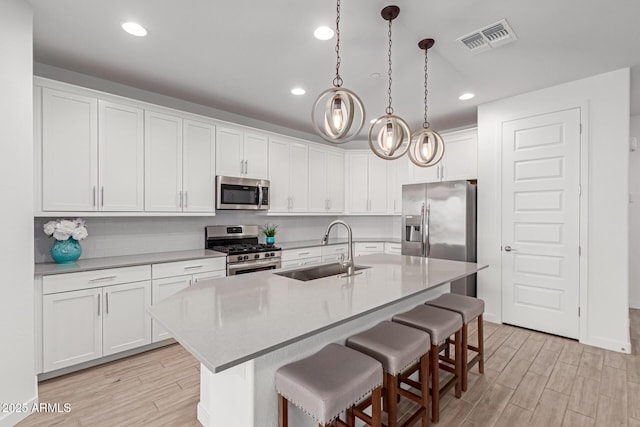 kitchen featuring light wood finished floors, visible vents, a kitchen breakfast bar, stainless steel appliances, and a sink