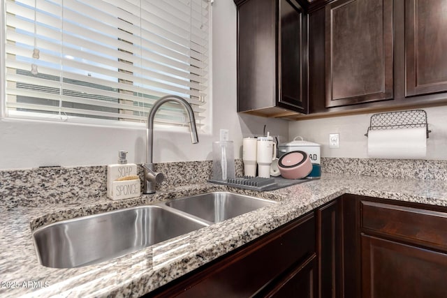 kitchen with light stone countertops, sink, and dark brown cabinets