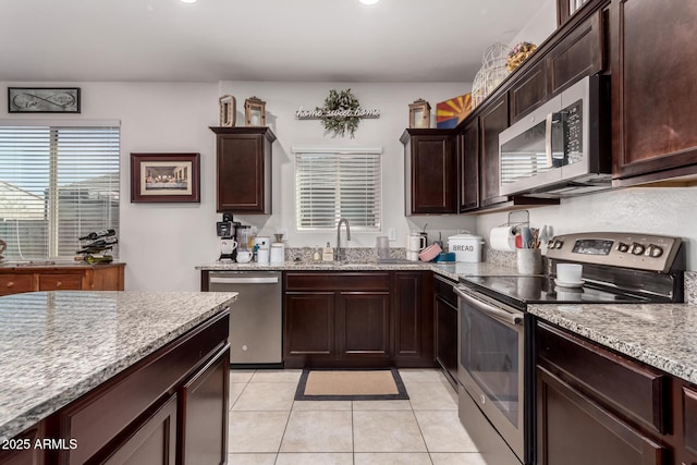 kitchen featuring light tile patterned flooring, sink, dark brown cabinets, stainless steel appliances, and light stone countertops