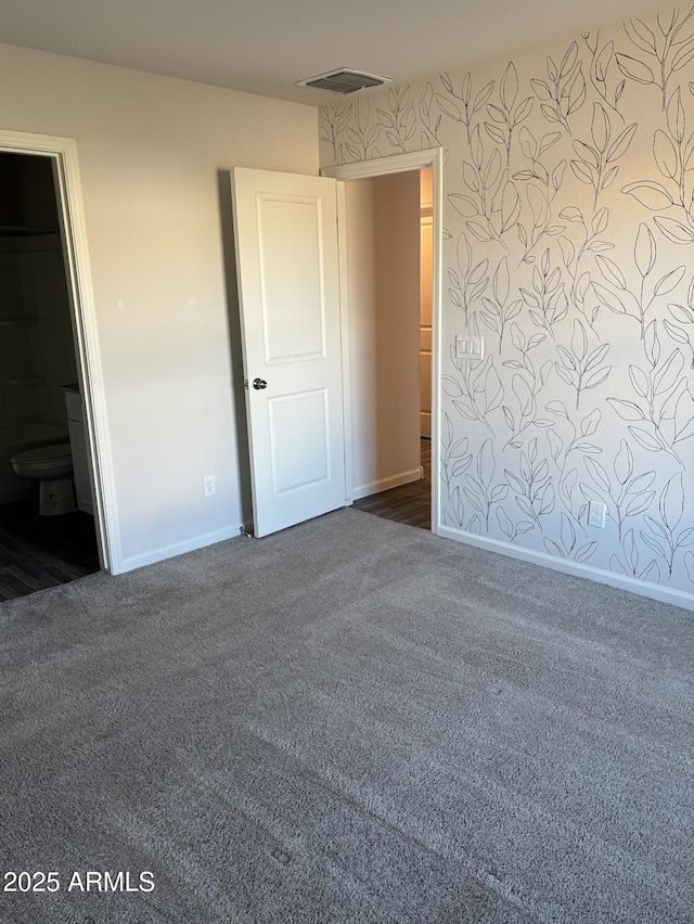 unfurnished bedroom featuring ensuite bathroom and dark carpet