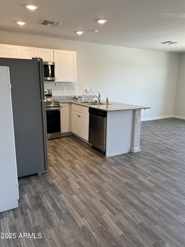 kitchen with light stone countertops, sink, dark wood-type flooring, stainless steel appliances, and white cabinets