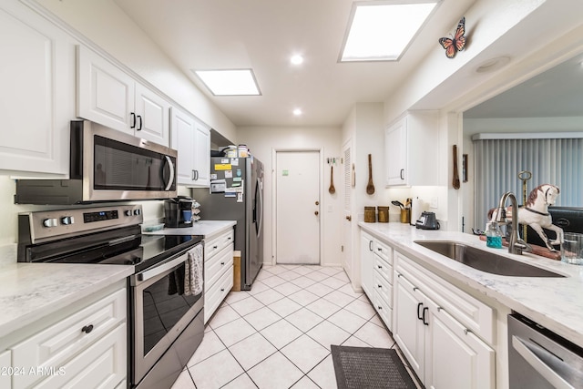 kitchen with a skylight, stainless steel appliances, sink, light tile patterned floors, and white cabinetry