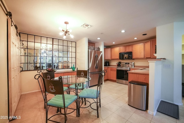 kitchen with a barn door, appliances with stainless steel finishes, light tile patterned floors, and a chandelier