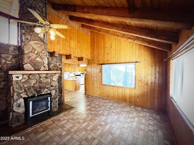 unfurnished living room with a stone fireplace, a wood stove, ceiling fan, lofted ceiling with beams, and wood ceiling