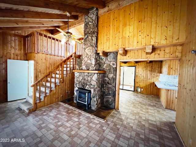 interior space with a wood stove, tile floors, ceiling fan, wooden walls, and lofted ceiling with beams