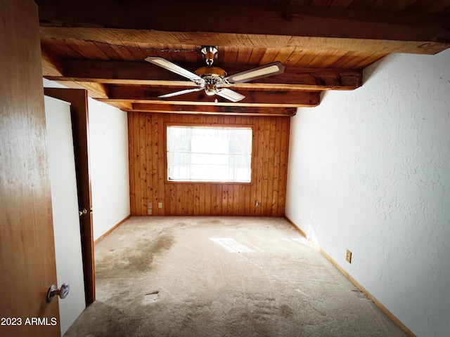 spare room featuring ceiling fan, wooden walls, beam ceiling, wood ceiling, and light carpet