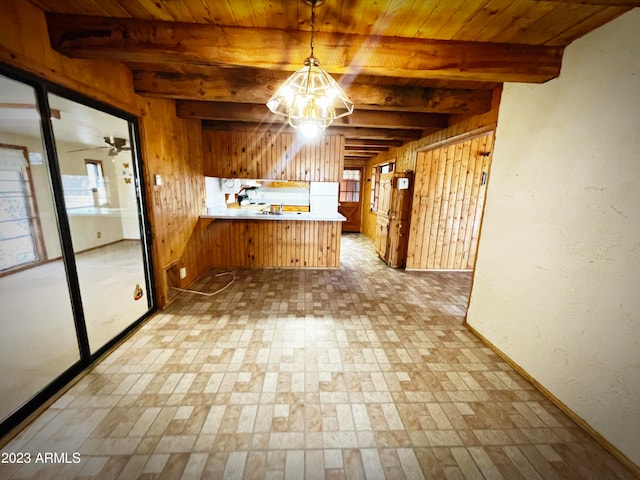 kitchen with kitchen peninsula, wooden walls, pendant lighting, ceiling fan with notable chandelier, and beam ceiling