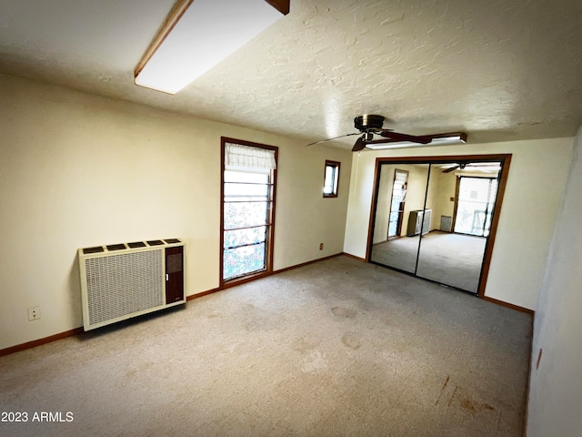 carpeted spare room with a textured ceiling, radiator heating unit, and ceiling fan