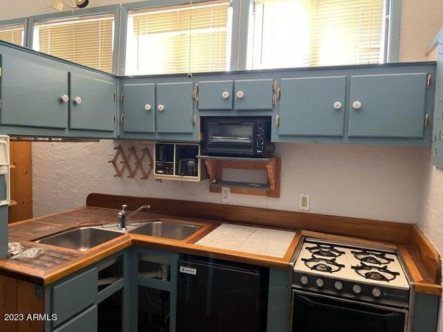 kitchen featuring white gas range, tile counters, sink, and blue cabinetry