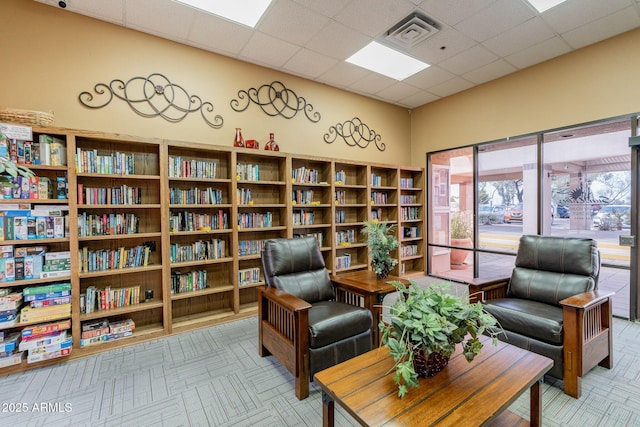living area featuring visible vents, a paneled ceiling, and bookshelves