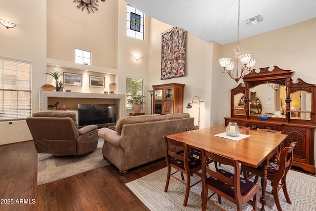 dining area featuring visible vents, a glass covered fireplace, a high ceiling, a chandelier, and dark wood-style flooring