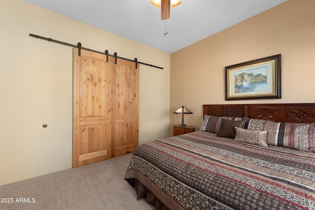 carpeted bedroom featuring a barn door and ceiling fan