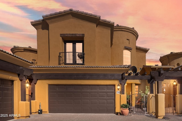 mediterranean / spanish home with stucco siding, a garage, a balcony, driveway, and a gate