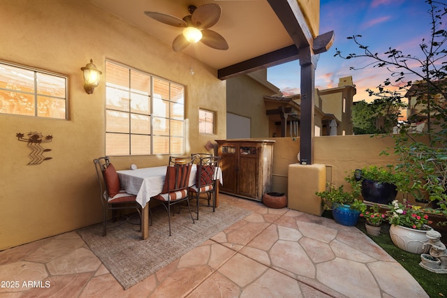 patio terrace at dusk featuring a ceiling fan and fence