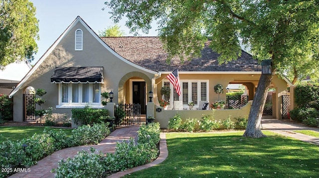 tudor home with a front yard, a fenced front yard, a gate, and stucco siding