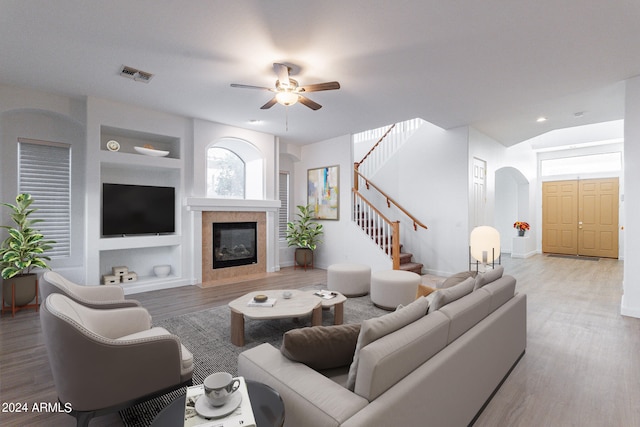 living room featuring hardwood / wood-style flooring, ceiling fan, built in features, a tile fireplace, and vaulted ceiling