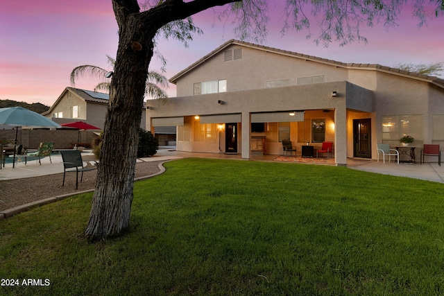 back of property at dusk featuring a lawn, fence, stucco siding, and a patio area
