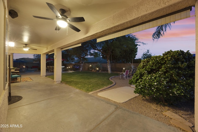 patio terrace at dusk with a lawn, a ceiling fan, and a fenced backyard