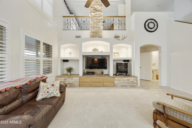carpeted living room with a wood stove, a ceiling fan, baseboards, a towering ceiling, and visible vents
