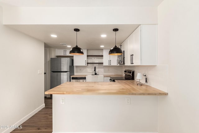 kitchen featuring stainless steel appliances, white cabinets, wood counters, decorative light fixtures, and kitchen peninsula