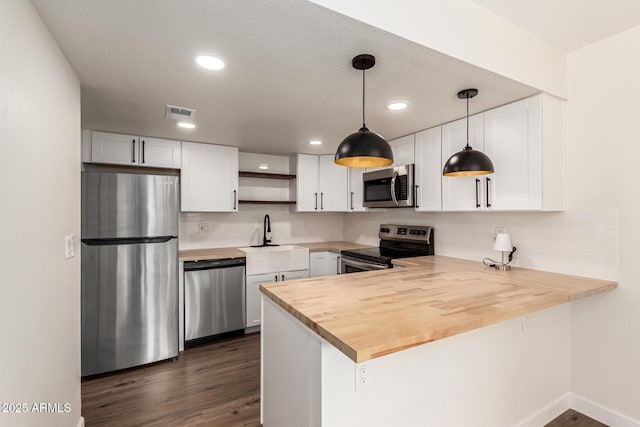 kitchen with butcher block countertops, kitchen peninsula, white cabinets, and appliances with stainless steel finishes