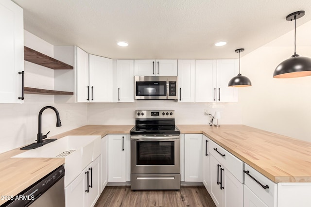 kitchen featuring sink, butcher block counters, stainless steel appliances, white cabinets, and decorative light fixtures