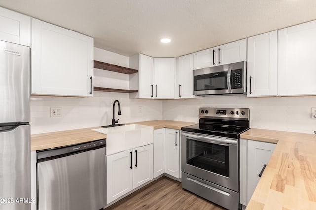 kitchen with wood counters, white cabinetry, sink, stainless steel appliances, and dark wood-type flooring